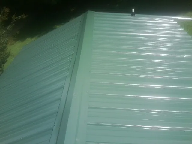 New green metal panels meeting at the ridge of a roof — Flat Roof Repair work by our crew in Corunna