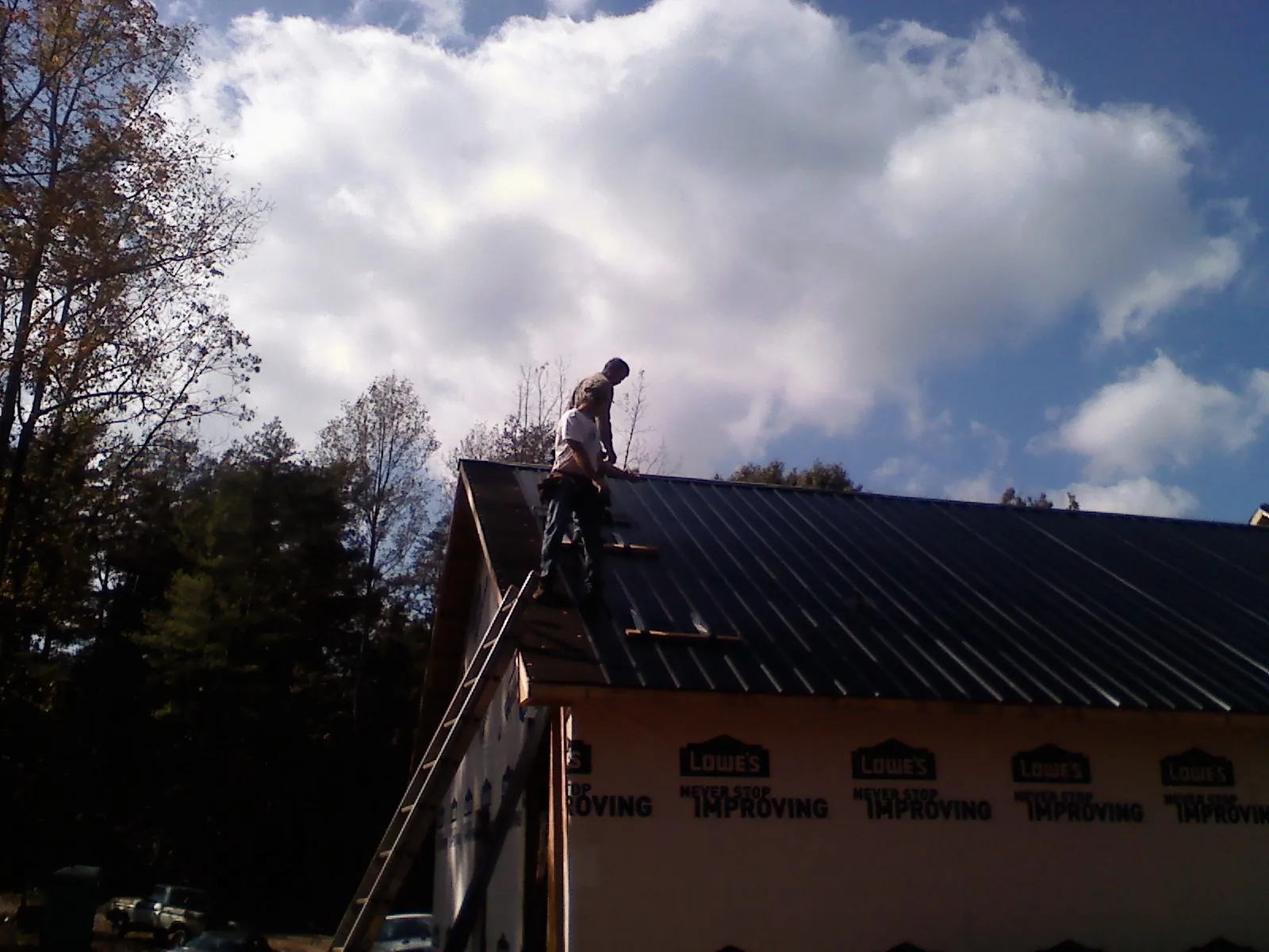 Roofer fastening dark metal panels high against a cloudy sky, from a Roof Inspection job in Corunna