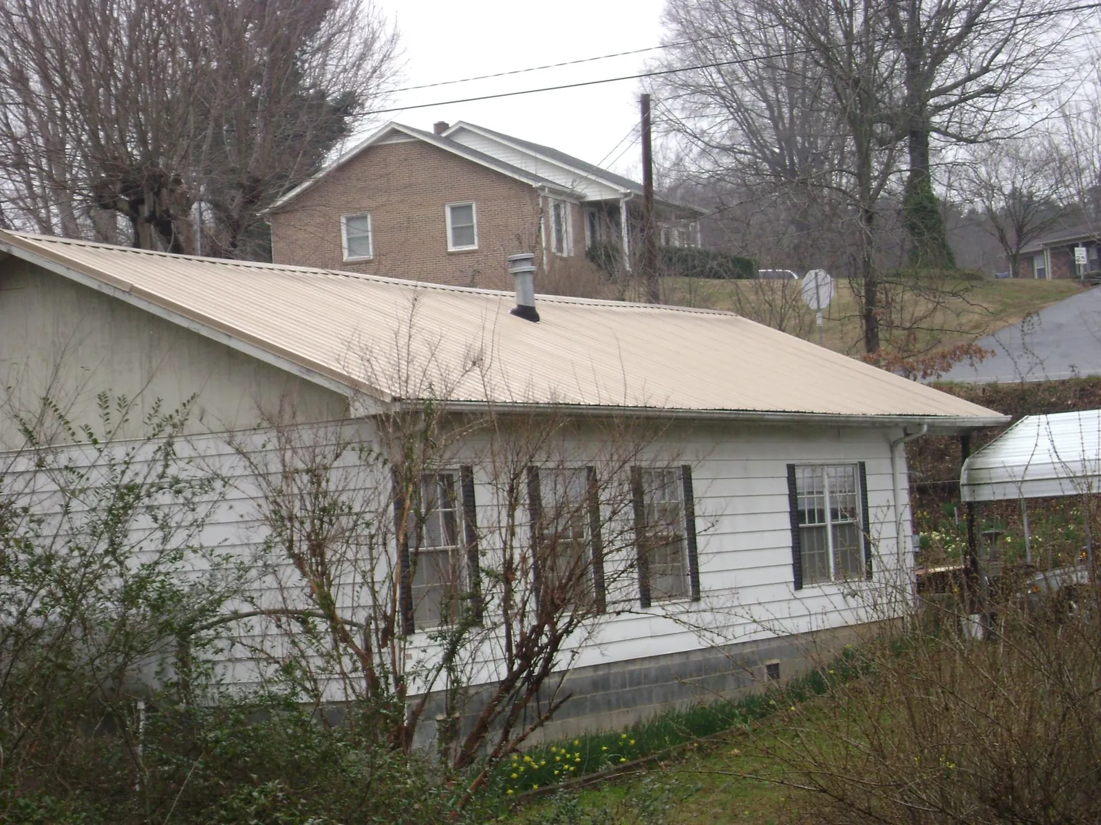 Tan metal roof on a white sided house set into a hillside — Commercial Roofing by Roofing Brothers in Corunna