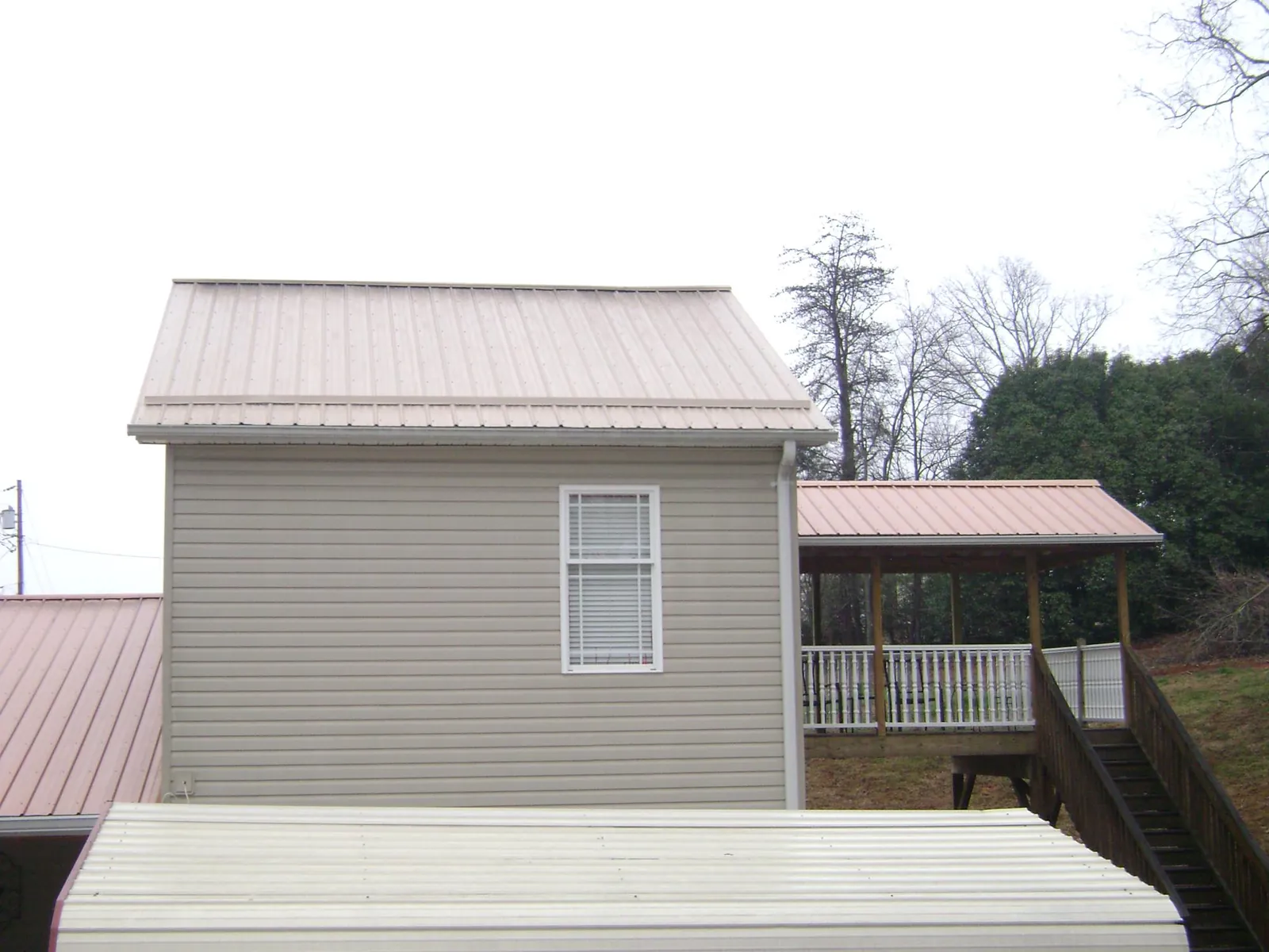 Tan metal roofs on a two story addition and attached porch, from a Roof Replacement job in Corunna